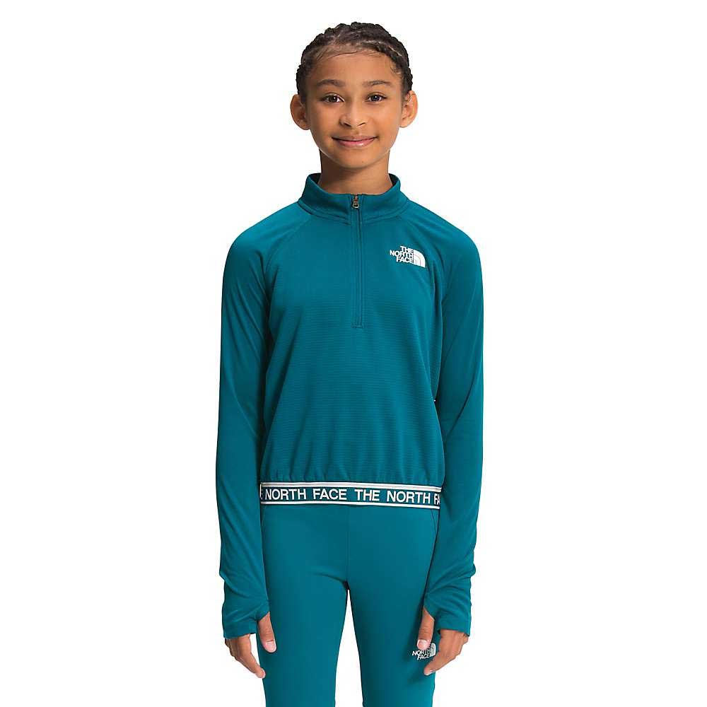 A young girl in a teal The North Face Girls Reactor Thermal 1/4 Zip Top, made with recycled polyester, and matching pants stands facing forward, smiling against a plain white background.