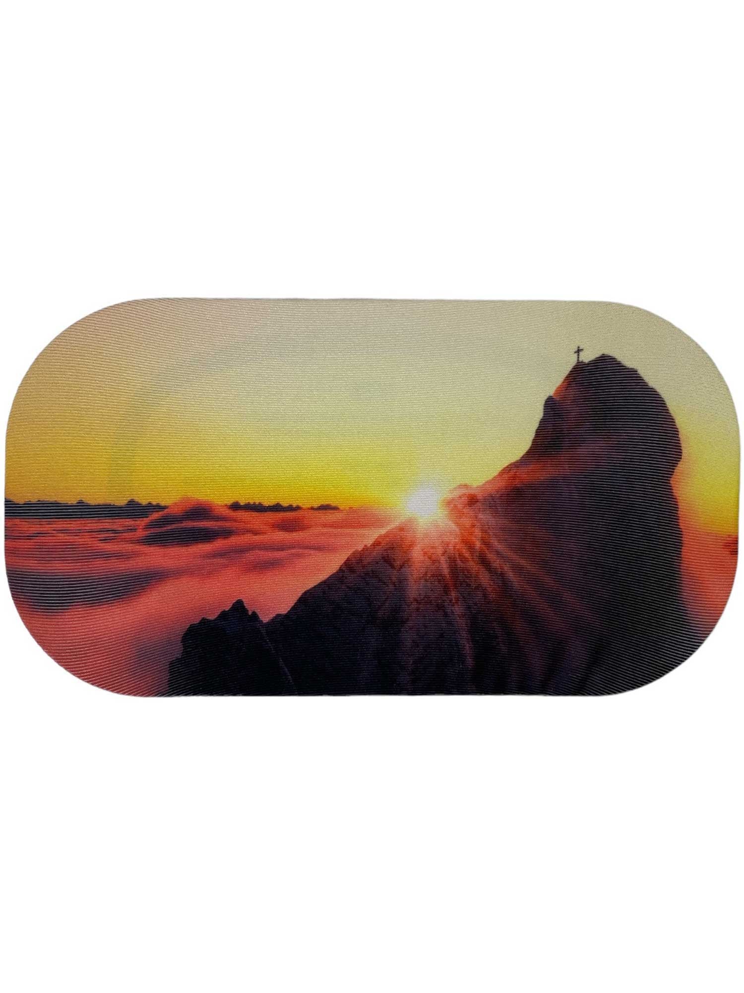 A mountain peak crowned with a cross soars above sunrise clouds, sunbeams streaming—an inspiring view for adventurers searching for eco-friendly gear like the GoggleSoc Protective Goggle Cover.