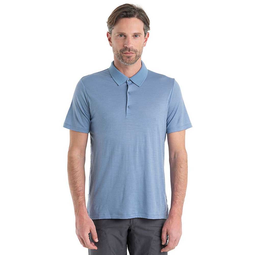 A man with short brown hair and light stubble is wearing the Icebreaker Mens Tech Lite II SS Polo in light blue, paired with dark pants, standing facing forward against a plain white background.