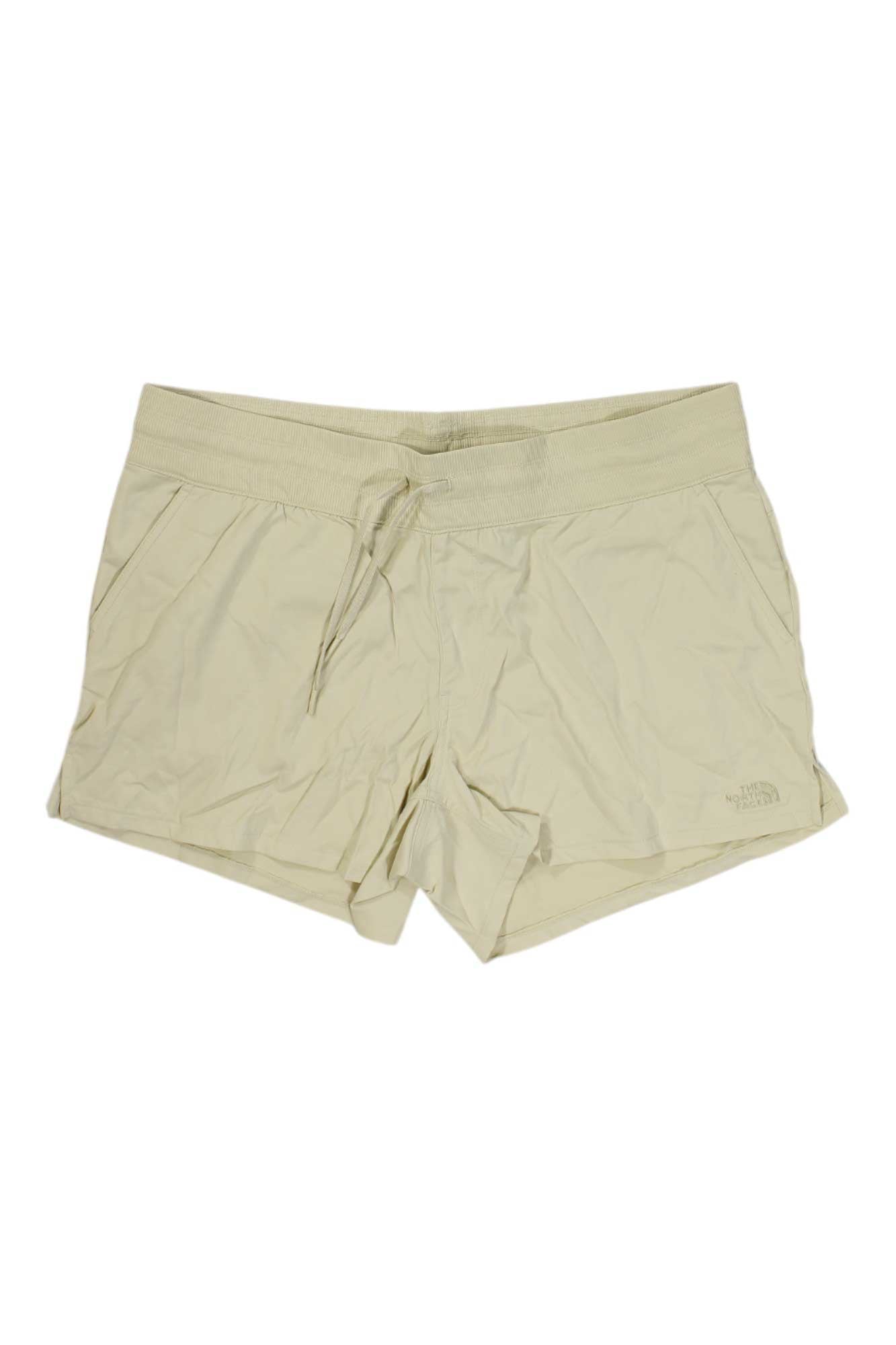 The North Face Womens Aphrodite Motion 4 Inch Short, shown in beige on a white background, features a lightweight design, elastic waistband with drawstring tie, four-way stretch fabric, and side pockets.