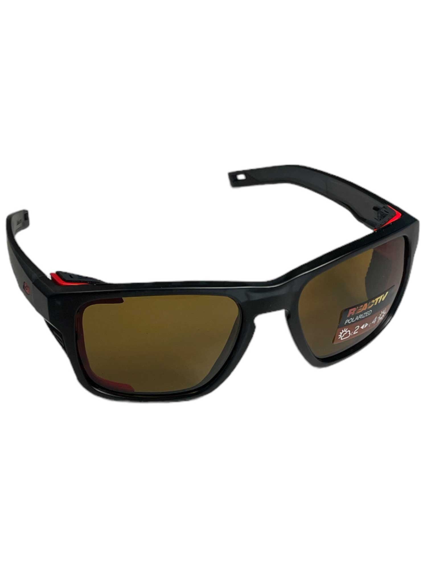 Shield M sunglasses with wraparound dark frames, brown lenses, and red side details.
