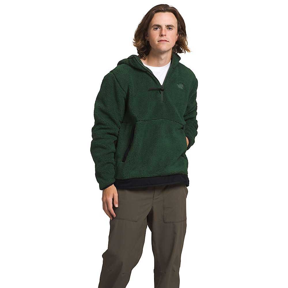 A person with shoulder-length brown hair wears The North Face Mens Campshire Fleece Hoodie and olive green pants while standing against a plain white background.