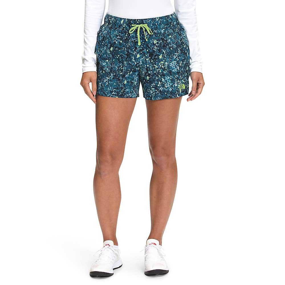 A person wearing a white long-sleeve shirt, The North Face Womens Printed Class V 4 Inch Short with a blue pattern and yellow drawstring, and white sneakers stands facing forward against a plain white background.