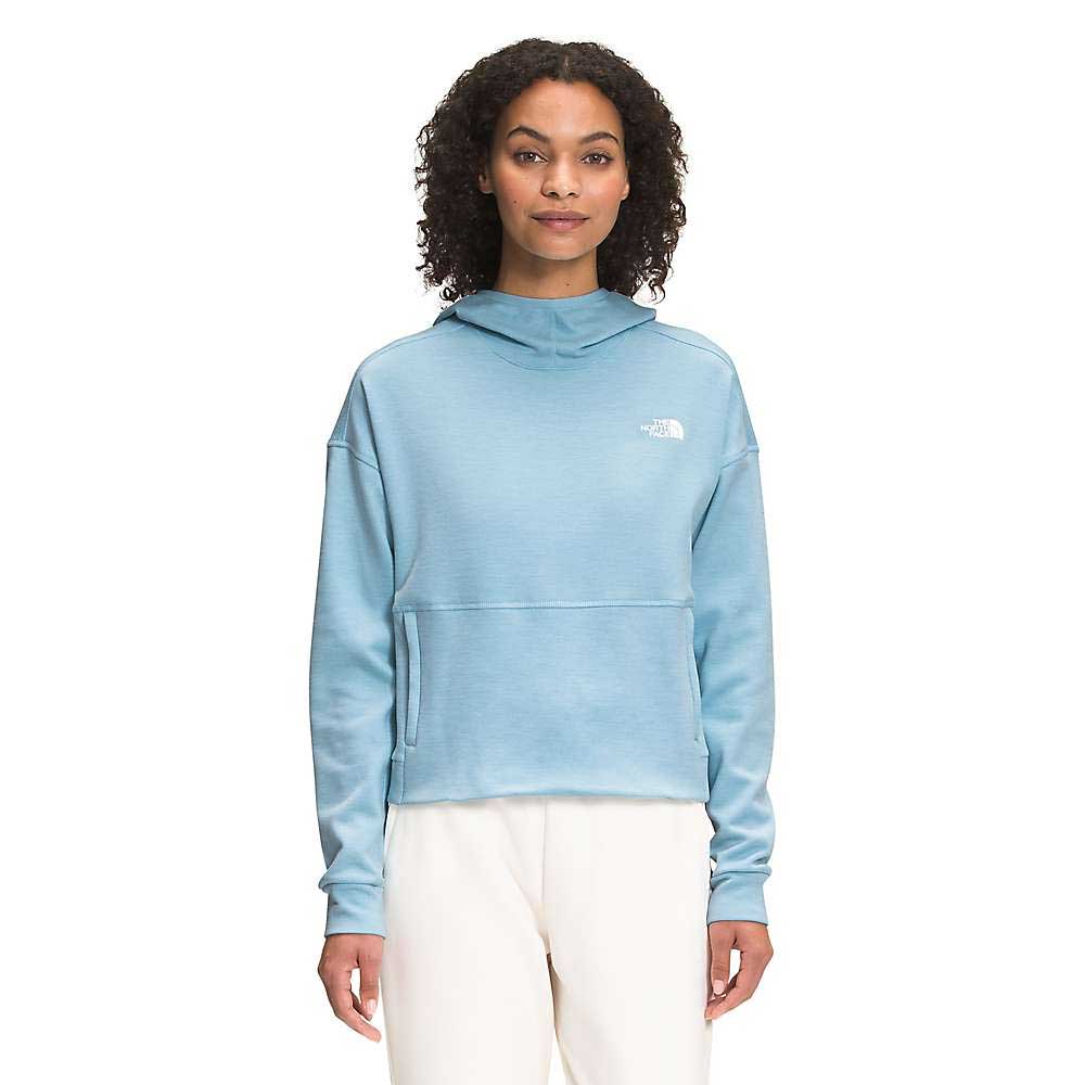 A woman with curly hair wears The North Face Womens Canyonlands Pullover Crop in light blue with white pants, standing against a plain white background.