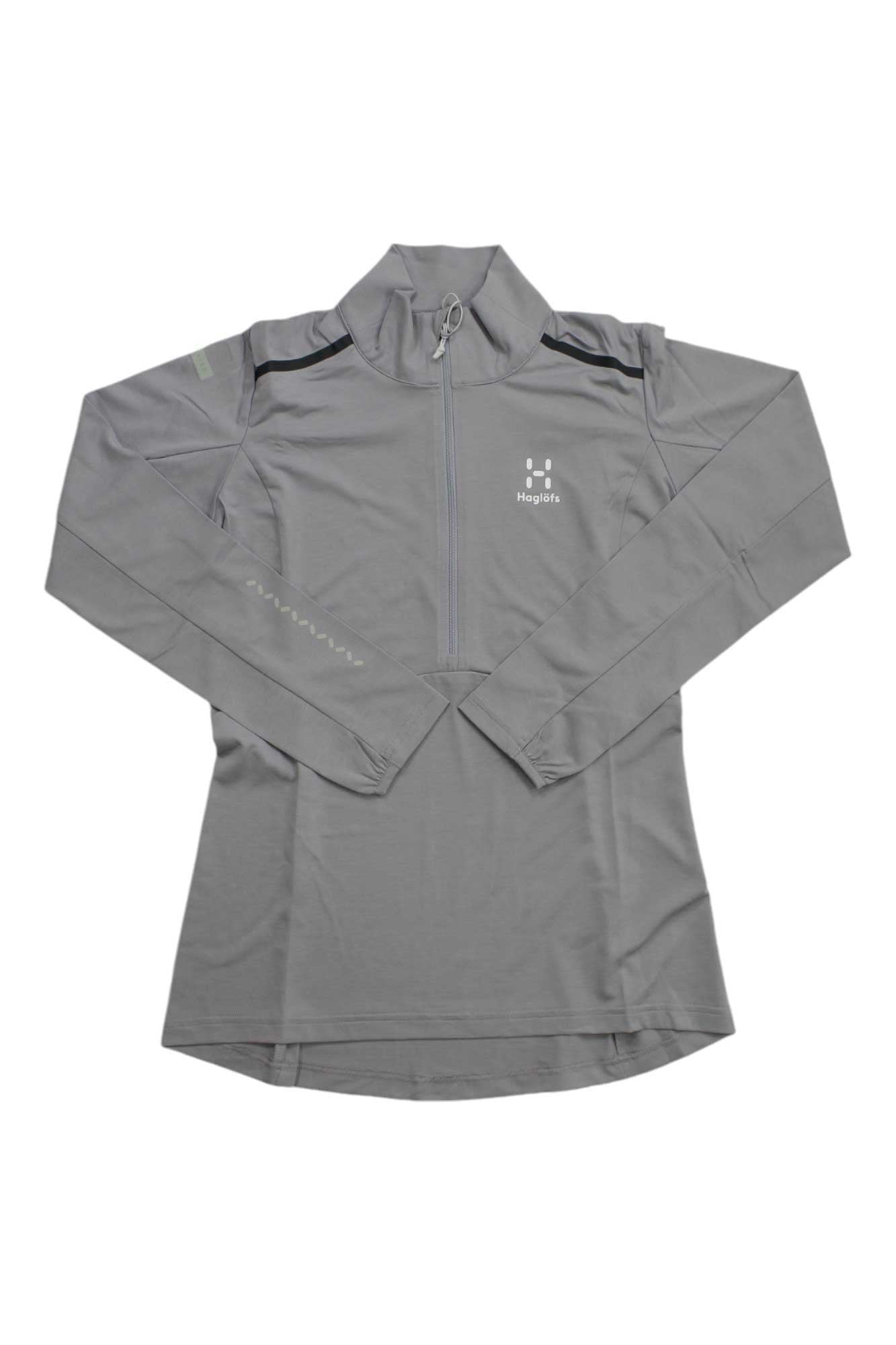 The Haglofs Womens L.I.M Strive Mid Top is a light gray, long-sleeve hiking top with a half-zip front, high collar, small white logo, and subtle seam details. Made from lightweight recycled polyester and bluesign approved with a curved hem.