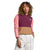 A woman with curly hair wears The North Face Womens Mountain Sweatshirt Pullover in color-blocked burgundy, pink, and tan with white pants, standing against a plain white background with one hand in her pocket.