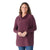 Smiling woman with long curly hair wears the Smartwool Womens Edgewood Poncho Sweater in plum and blue jeans, standing against a plain white background.