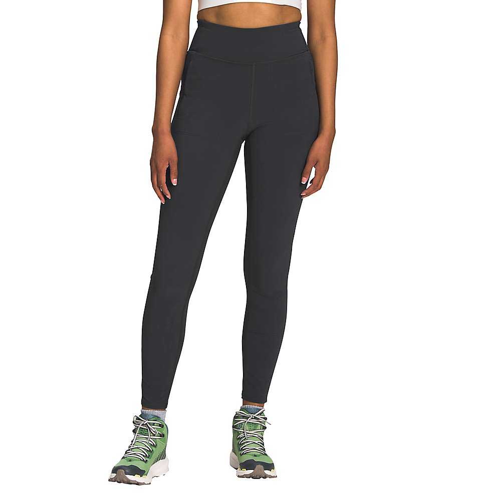 A person wearing The North Face Womens Bridgeway Hybrid Tight high-waisted fitness pants in black and green hiking shoes stands against a plain white background. Only the lower body is visible; the upper body and head are cropped out.