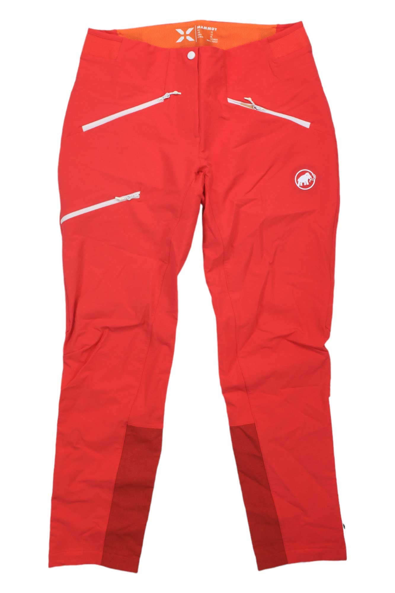 The Mammut Womens Eisfeld Advanced SO Pants are red climbing pants for women, featuring multiple zippered pockets, a white logo on the left thigh, reinforced inner ankles, and an orange waistband. Shown laid flat on a white background.