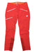 The Mammut Womens Eisfeld Advanced SO Pants are red climbing pants for women, featuring multiple zippered pockets, a white logo on the left thigh, reinforced inner ankles, and an orange waistband. Shown laid flat on a white background.