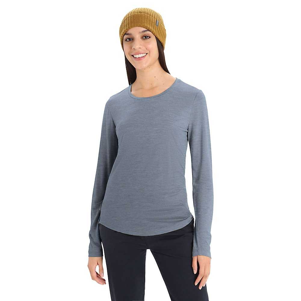 A smiling woman wears a mustard yellow knit beanie, black pants, and the Icebreaker Womens Sphere II LS Tee, made from soft merino wool, standing against a plain white background.