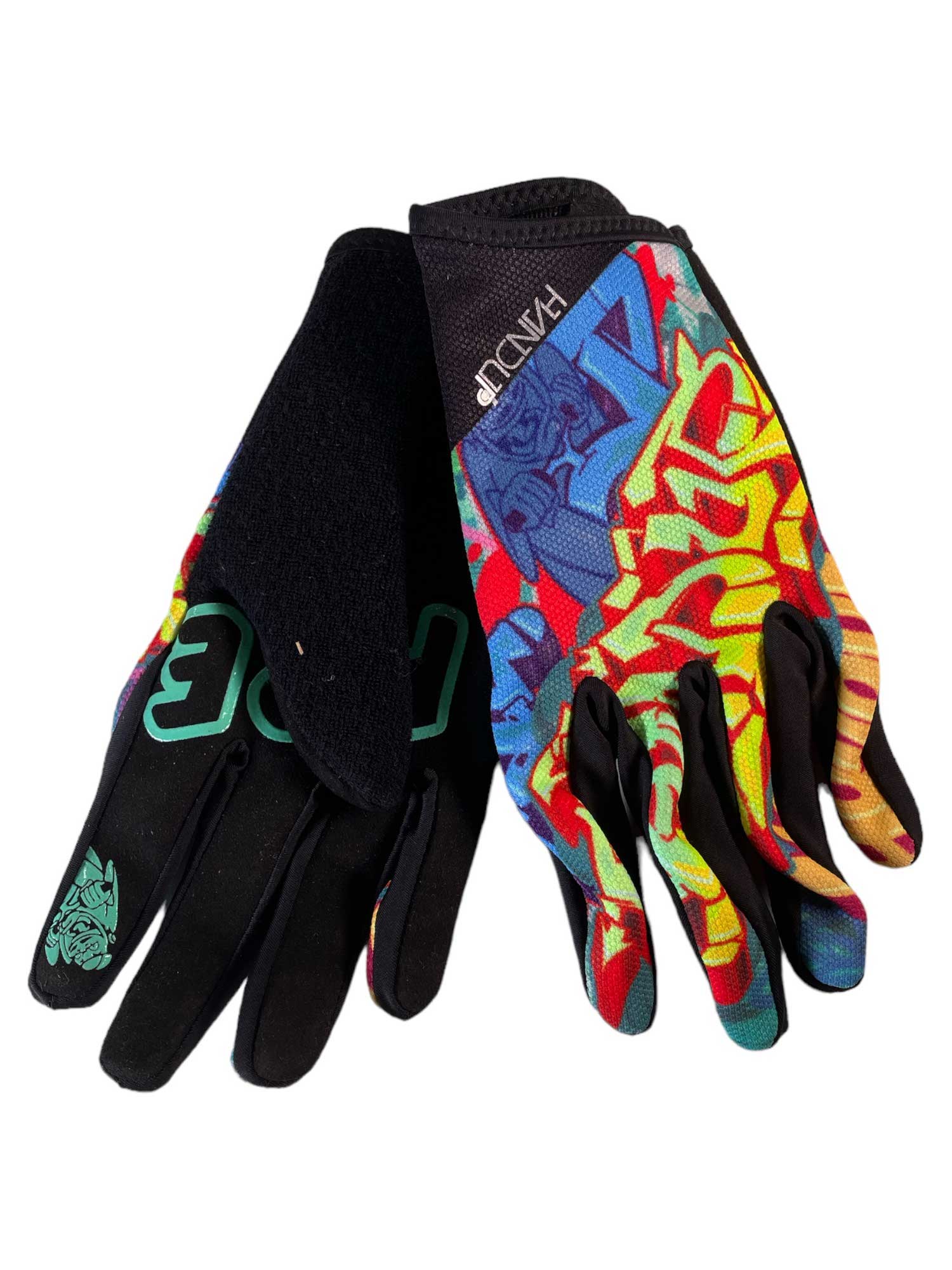The Handup Glove is a mountain biking glove with red, yellow, and blue graffiti-style patterns on top, black Clarino leather palms, green lettering on one glove, and a small mask graphic near the wrist.