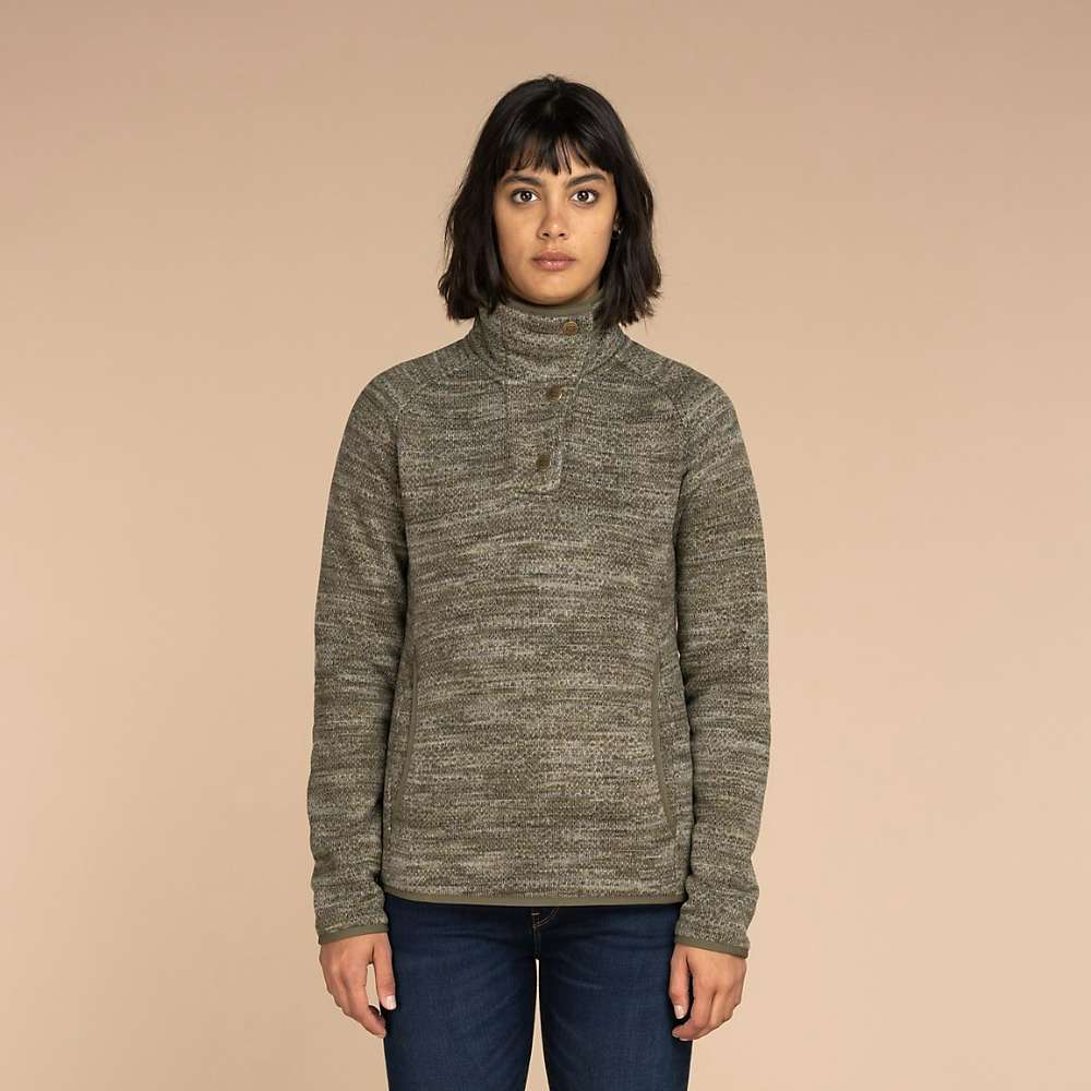 A woman with dark hair wears the Sherpa Women's Lumbini Pullover - Evergreen Texture, featuring Nepal-inspired trims and recycled polyester, standing facing forward against a plain beige background.