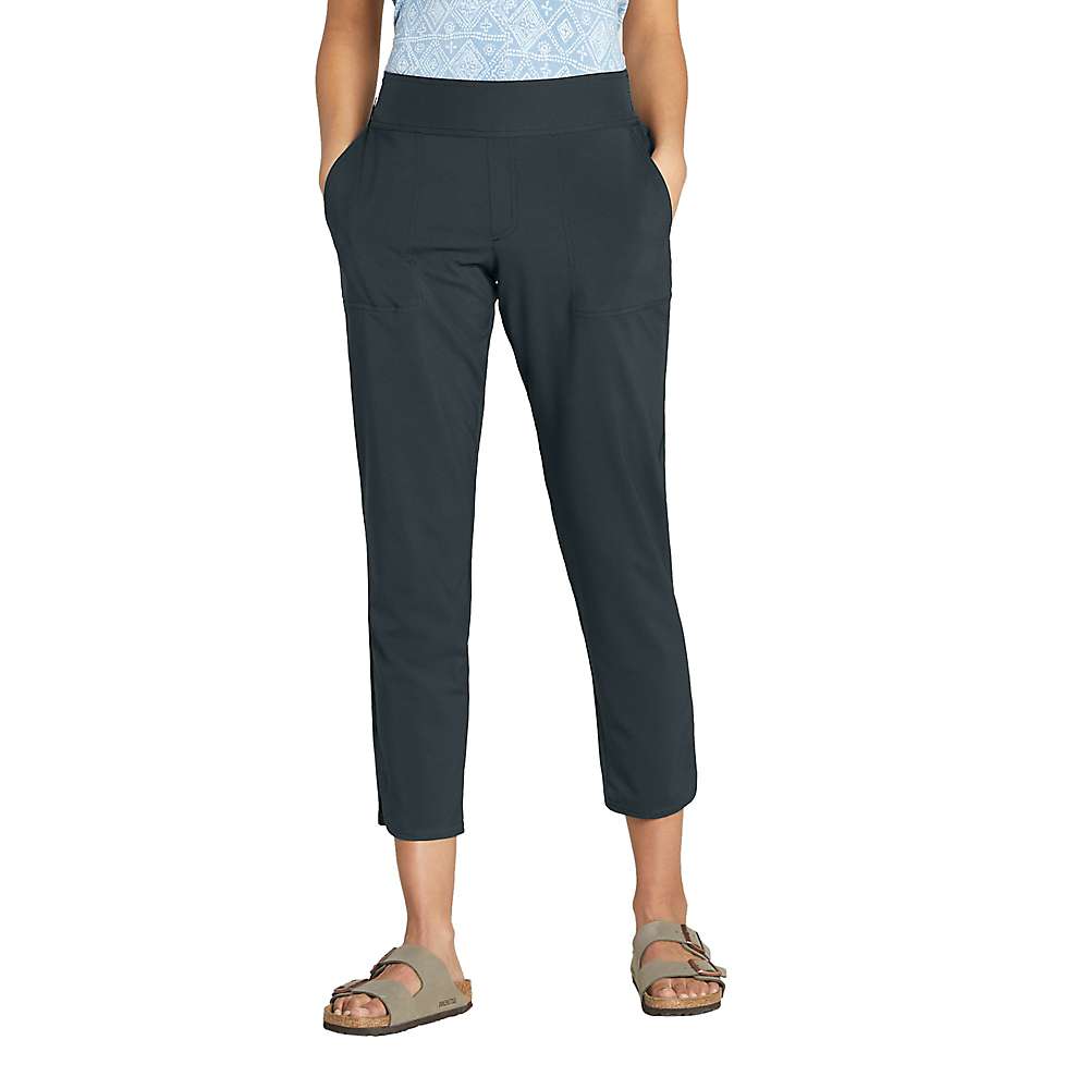 A person wears Sherpa Women's Sajilo Ankle Pant - Black XL with a light blue patterned top and tan sandals, standing hands-in-pockets against a white background. These quick-dry, UPF 50 pants offer style and all-day comfort.