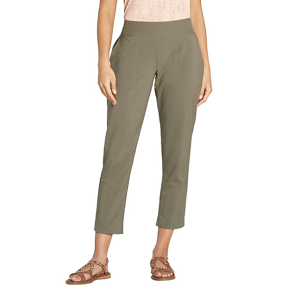 A person wearing Sherpa Women's Sajilo Ankle Pants - Evergreen, a peach patterned top, and brown sandals stands against a plain white background. The photo is cropped above the shoulders.