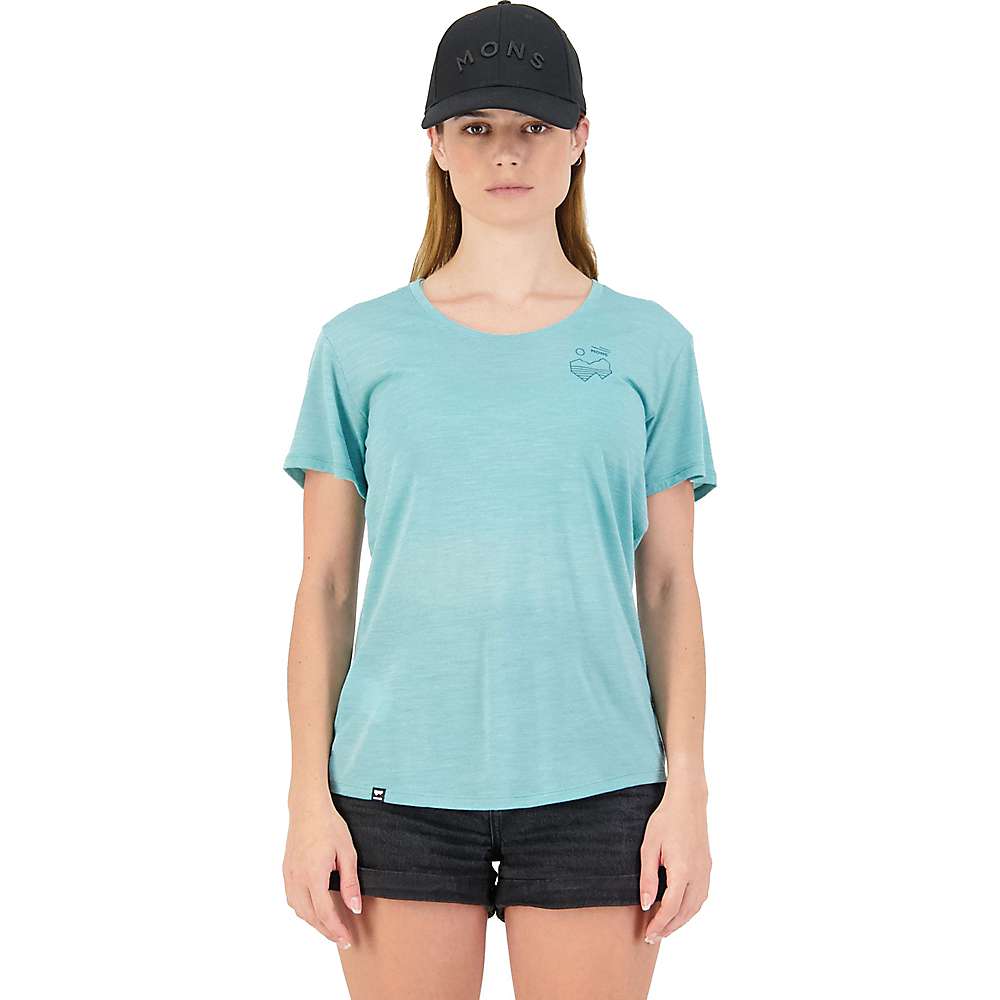 A woman faces forward, wearing a black cap, black shorts, and the Mons Royale Women's Zephyr Tee in Sage (size XS), an eco-friendly light blue shirt with a small graphic near the left shoulder. The background is plain white.