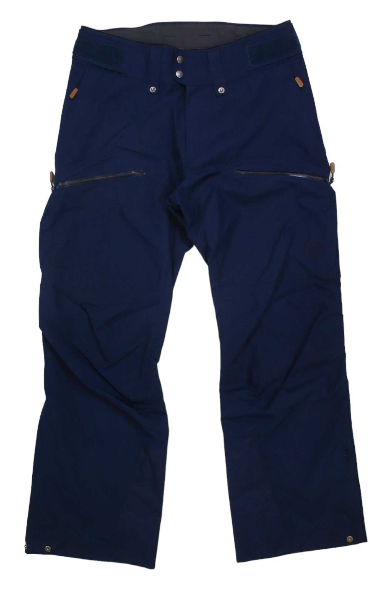 A pair of Norrona Men's Tamok GTX Pants in dark blue, featuring front zipper pockets, button closure, and belt loops, is laid flat on a white background.