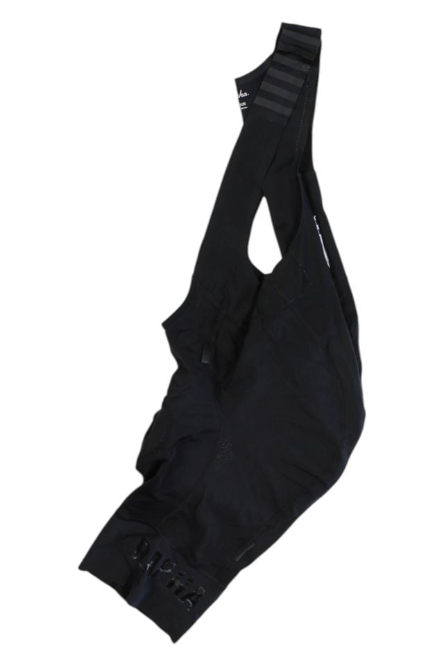 A pair of black Rapha Mens Pro Team Bib Shorts II - Regular with straps, race-grade chamois, subtle branding, and a minimalist design is laid flat on a white background.