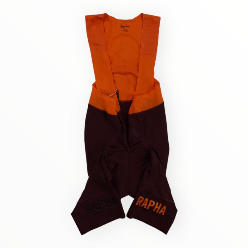 The Rapha Mens Pro Team Bib Shorts II - Regular features orange shoulder straps and upper, dark maroon lower section, RAPHA in orange on both legs, and a race-grade chamois for optimal comfort on intense rides.