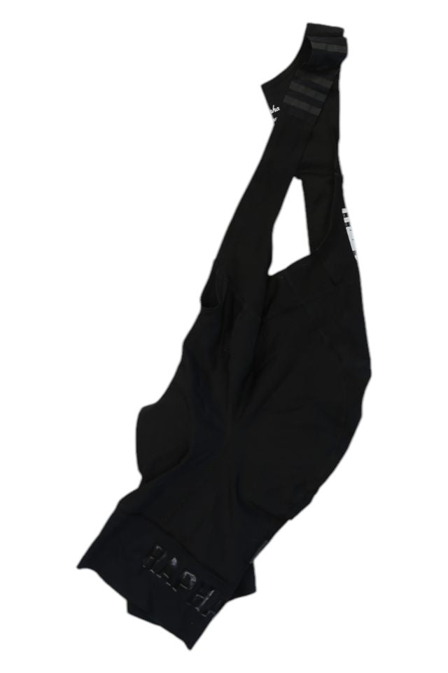 A pair of Rapha Mens Pro Team Bib Shorts II - Regular with race-grade chamois and shoulder straps is laid flat on a white background, showcasing smooth, fitted fabric and subtle branding near the leg openings.