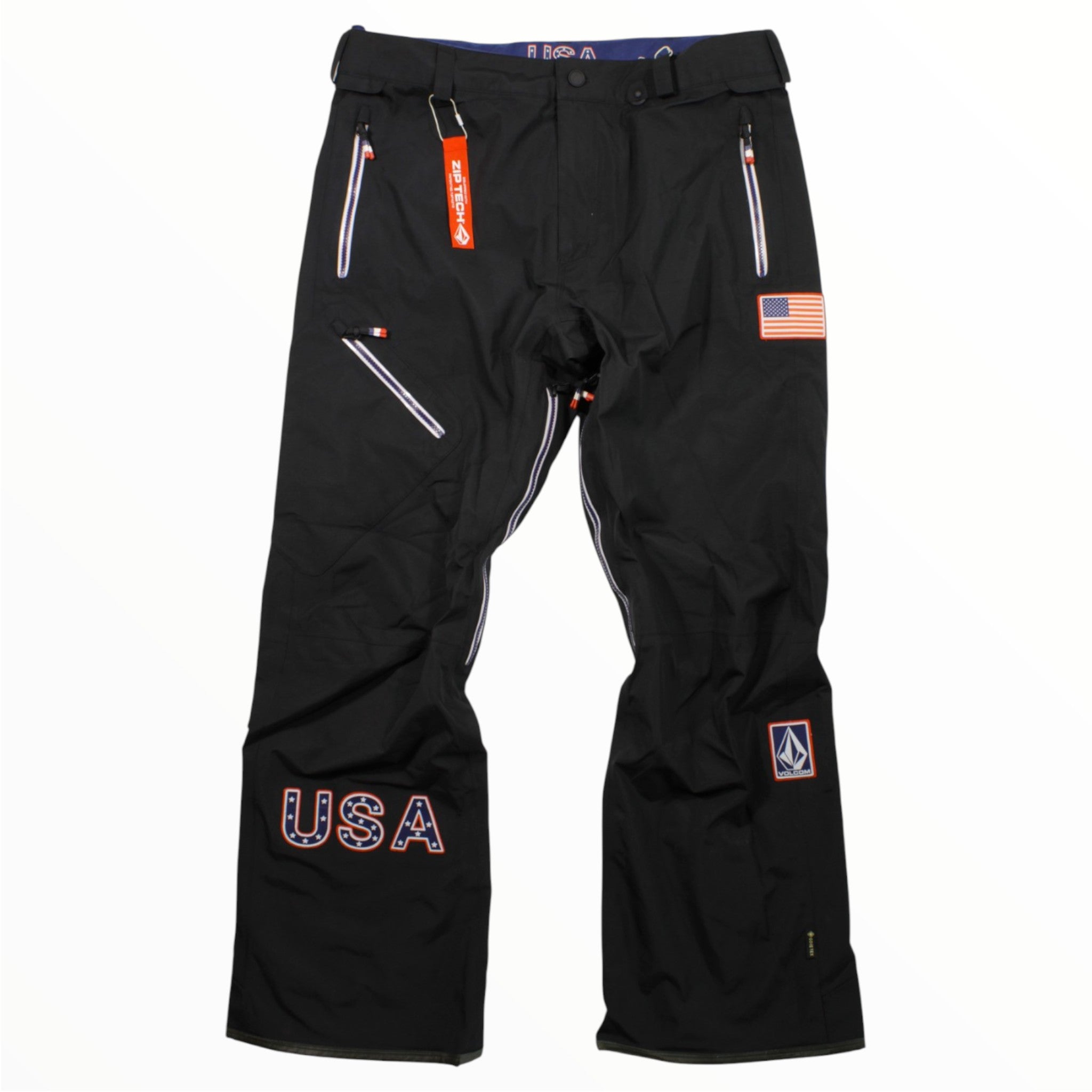 Volcom Mens Team USA GTX Snow Pants: Black waterproof ski pants featuring a USA flag and lettering on the left leg, white and red zippered pockets, Volcom logo patch, and a red belt loop tag for a sporty, patriotic look.