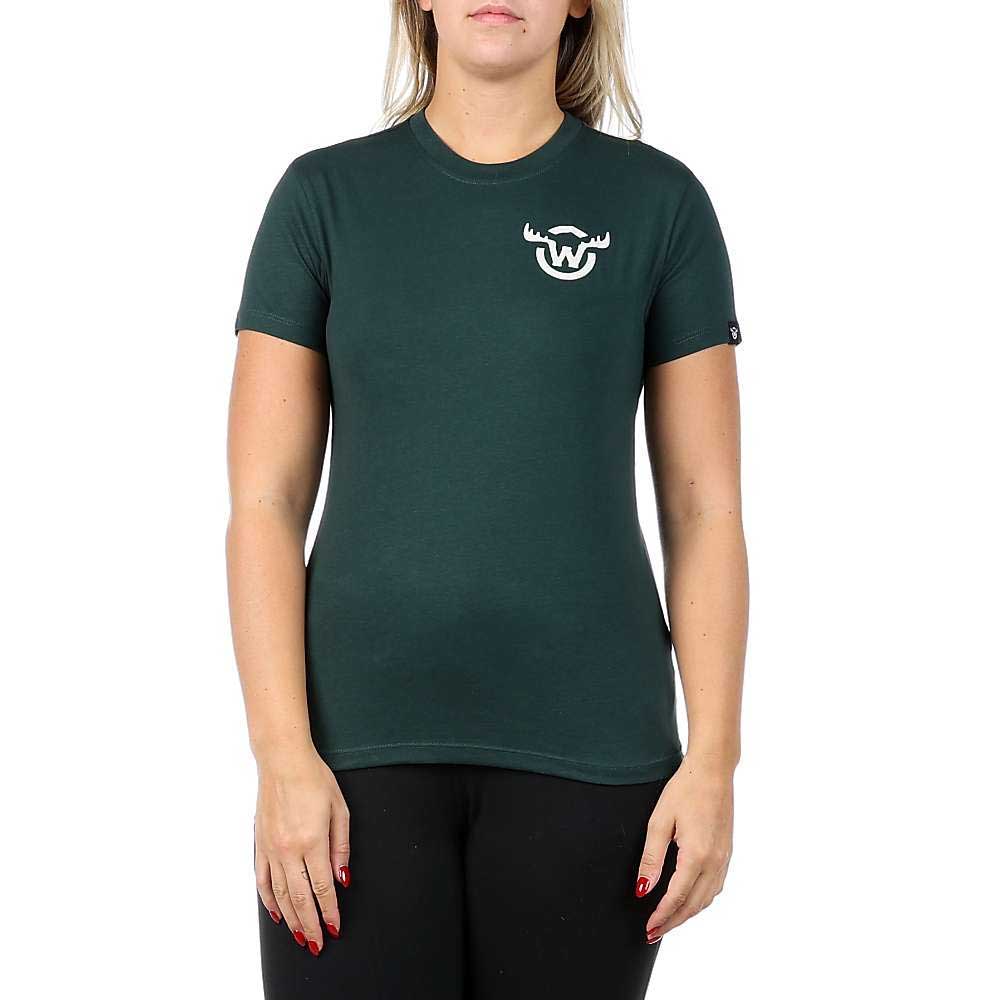 A person is wearing the Moosejaw Womens Fearsome Critter SS Tee, a dark green, organic cotton, short-sleeved shirt with a small white antlered W graphic on the left chest, paired with black pants and standing against a plain white background.
