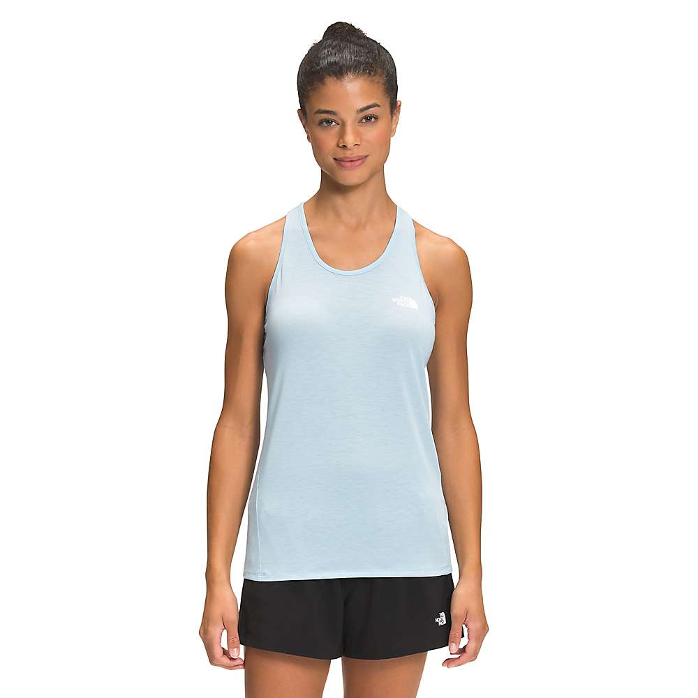 A woman faces forward wearing the Womens Wander Tank in light blue with black shorts, her dark hair tied in a bun, posing against a plain white background.