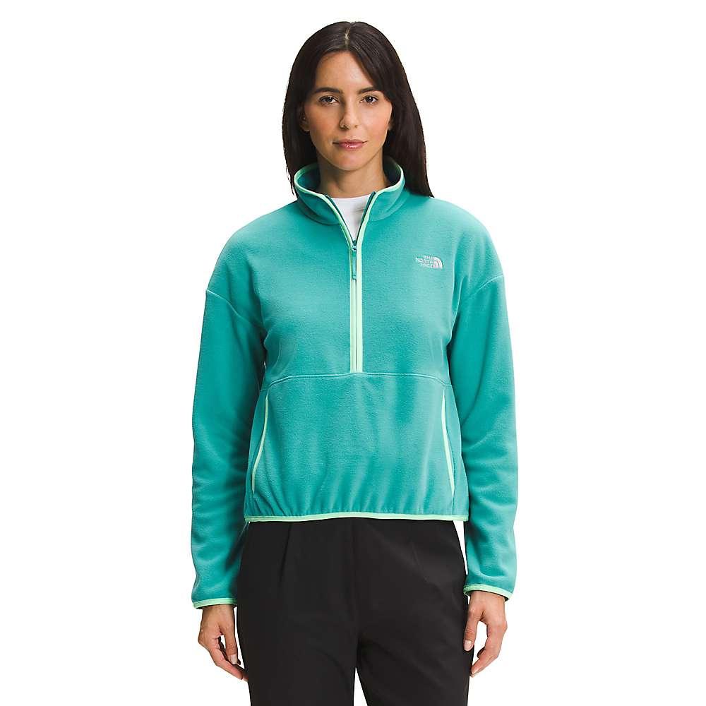 A woman faces forward, wearing The North Face Womens TKA Glacier Crop fleece in teal with white trim and black pants. The recycled polyester pullover displays a small white logo on the left chest, set against a plain white background.