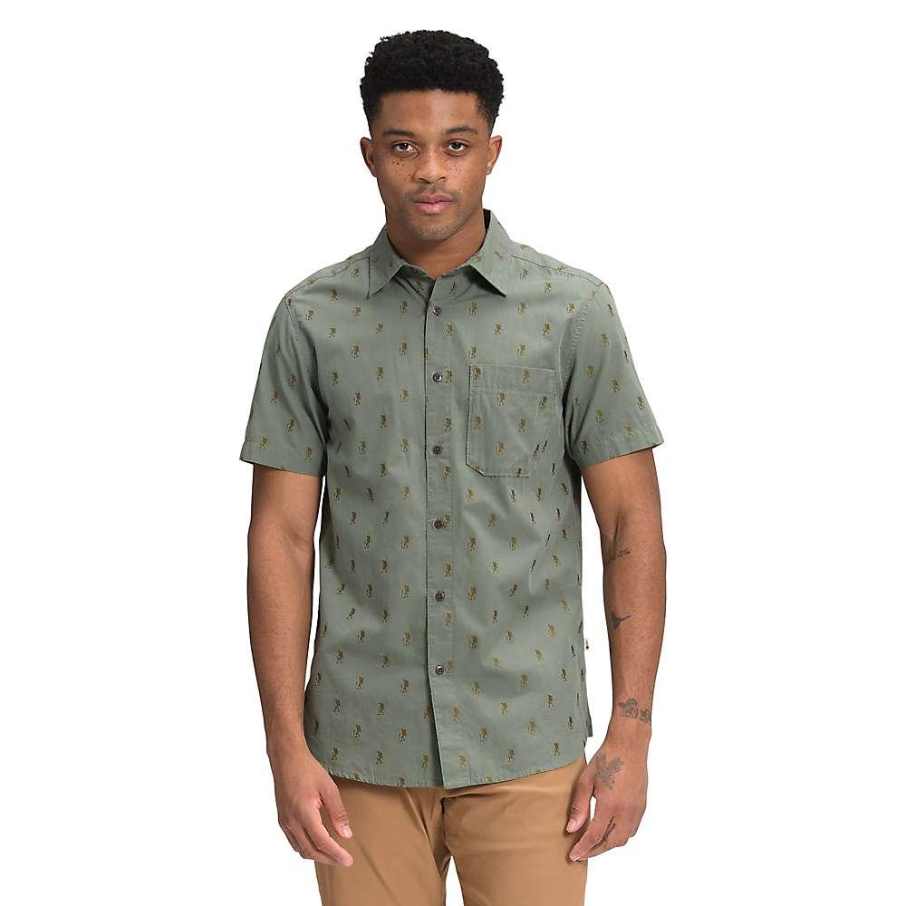 A man faces forward wearing The North Face Men's Baytrail Jacquard SS Shirt in sage green, featuring a subtle print, chest pocket, short sleeves, and classic button-up style. He pairs it with tan pants against a plain white background.