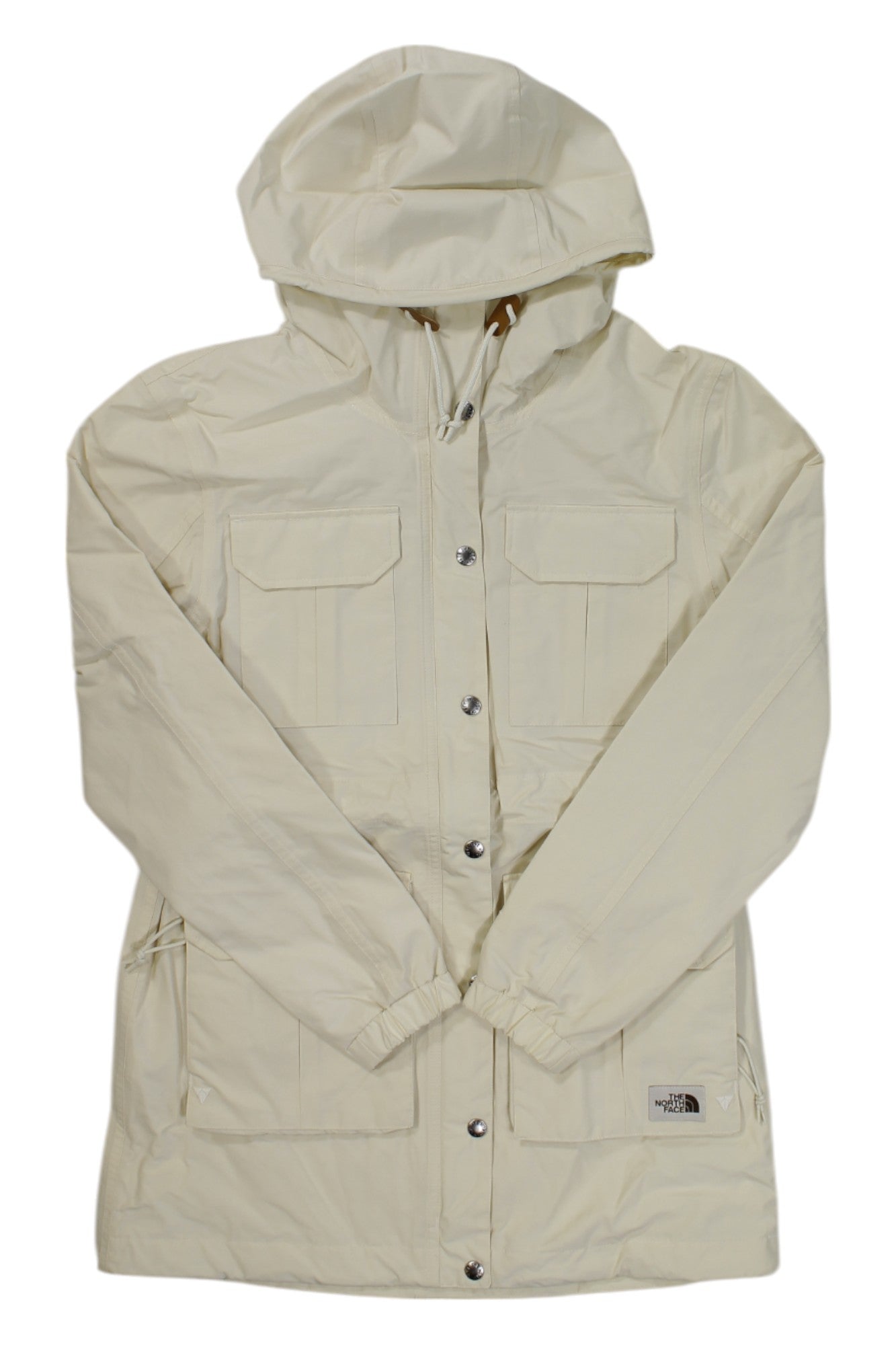 The Womens DryVent Mountain Parka is a cream-colored, waterproof jacket with snap buttons, front flap pockets, long sleeves, and The North Face logo patch near the bottom hem. It is shown flat on a white background.