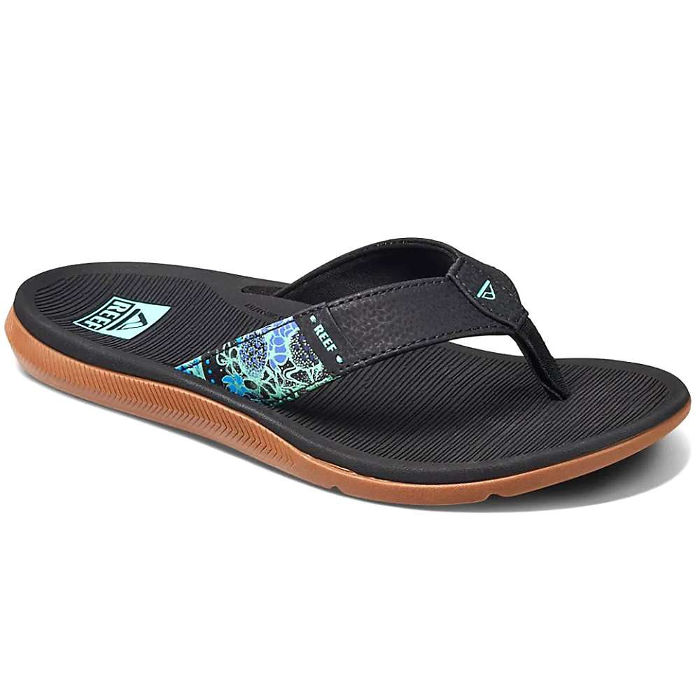 The Reef Womens Santa Ana Flip Flop features a black strap with blue and green patterned accents, a brown sole, textured footbed, water-friendly materials, arch support, and visible Reef logos on the strap and heel.