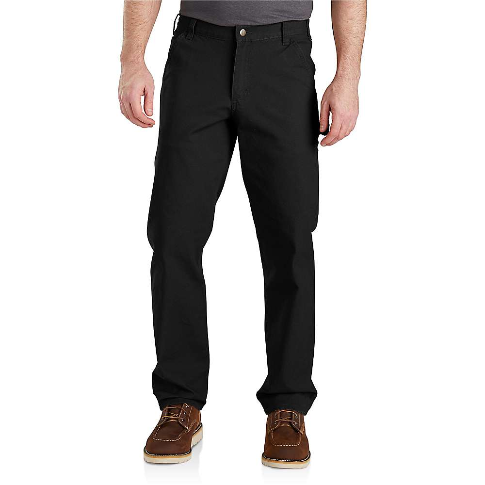 A man wears Carhartt Mens Rugged Flex Relaxed Fit Duck Dungaree black straight-leg pants, a dark gray shirt, and brown leather shoes against a white background. Only his body from the shoulders down is visible.