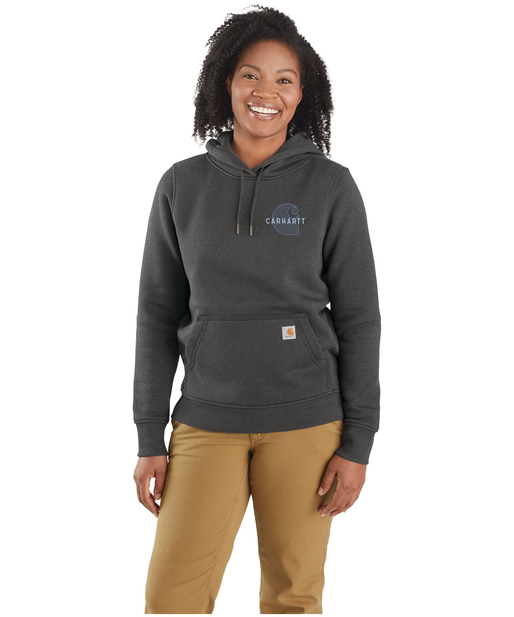 A smiling woman wears a dark grey Carhartt Womens Rain Defender Relaxed Fit Chest Graphic Sweatshirt and tan pants, standing against a plain white background.
