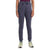 Only the lower half of a person is visible as they stand facing forward, wearing Icebreaker Womens Merino Crush II Pant in dark gray, a purple top, and light gray running shoes with green and yellow accents.