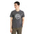 A person wearing the Icebreaker Men's Central Classic SS Tee - Move To Natural Mountain, a gray short sleeve tee with a circular mountain graphic, faces slightly to the side with one hand in their pants pocket.