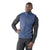 A man models the Smartwool Men's Smartloft Vest in blue over a dark long-sleeve shirt and black athletic pants, standing with one hand on his hip against a plain white background.