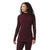 A woman with curly hair stands smiling to the side, wearing a maroon Smartwool Womens Thermal Merino Drape Neck Hoodie with long sleeves and front pockets.