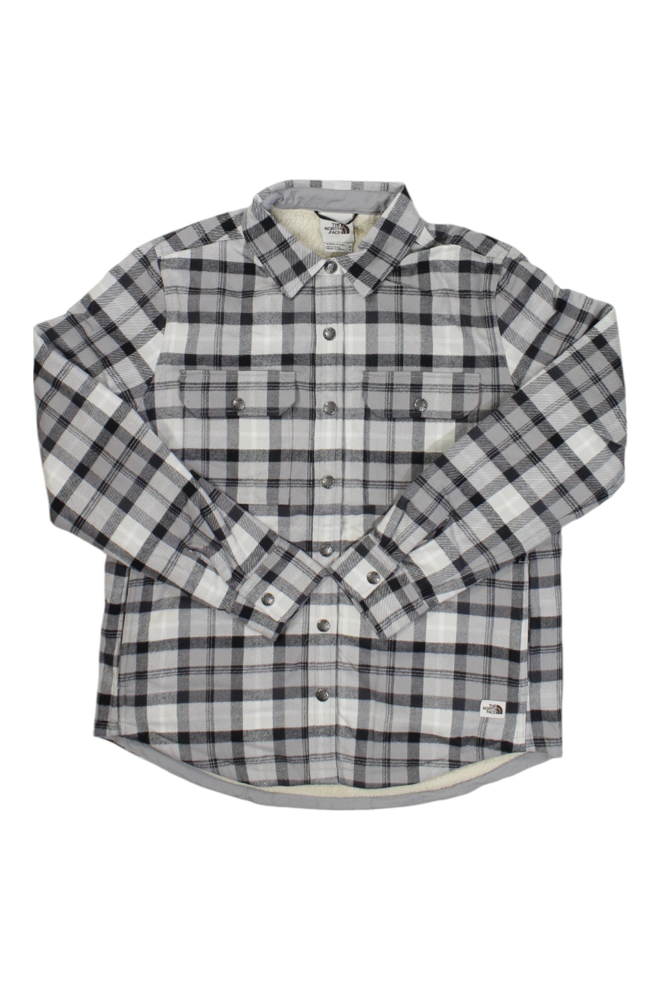 The North Face Womens Campshire Shirt is a long-sleeve, button-up made from soft organic cotton in a black, gray, and white plaid. It features two chest flap pockets with buttons and a small logo patch on the bottom left.