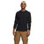 A man stands smiling against a plain white background, wearing The North Face Mens Canyon Fog Thermal LS Top in black, tan cargo pants, and a white backwards cap, with his right arm relaxed and his left hand in his pants pocket.