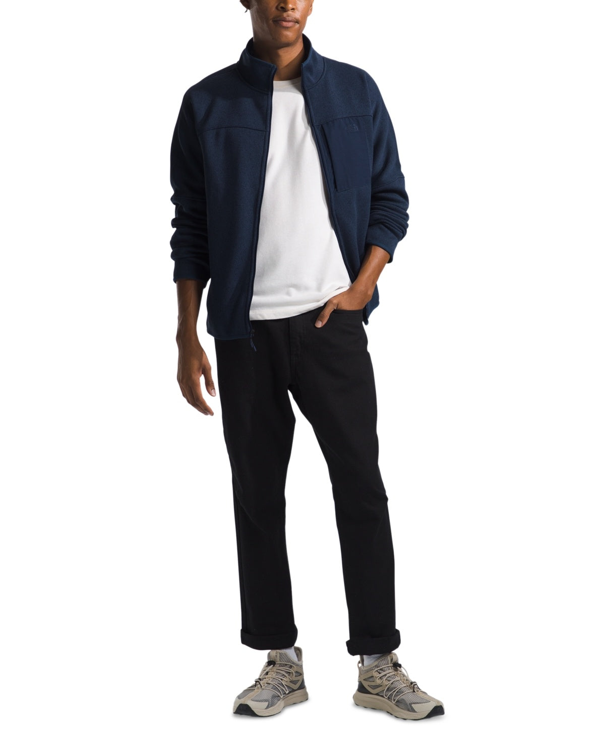 A person wearing The North Face Mens Front Range Fleece Jacket over a white shirt, black pants, and gray sneakers stands with one hand in their pocket against a white background.