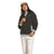 A person wearing a tan cap, The North Face Womens Campshire Fleece Jacket in dark fleece, a light blue shirt, and off-white pants stands with one hand in their pocket against a white background.