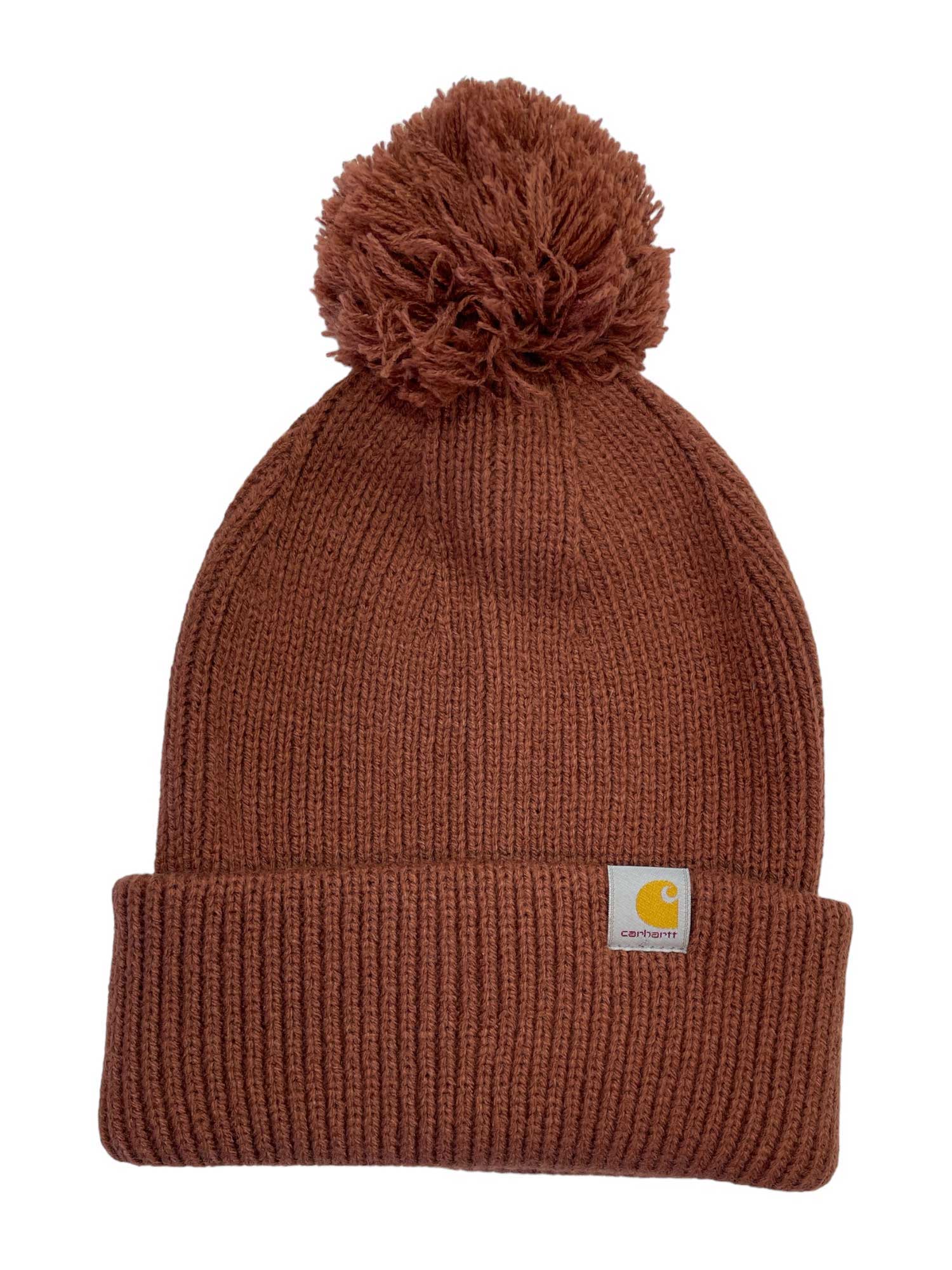 The Carhartt Womens Knit Pom Pom Cuffed Beanie is a brown knit hat with a large pom-pom on top, a folded brim, and a small Carhartt logo patch.