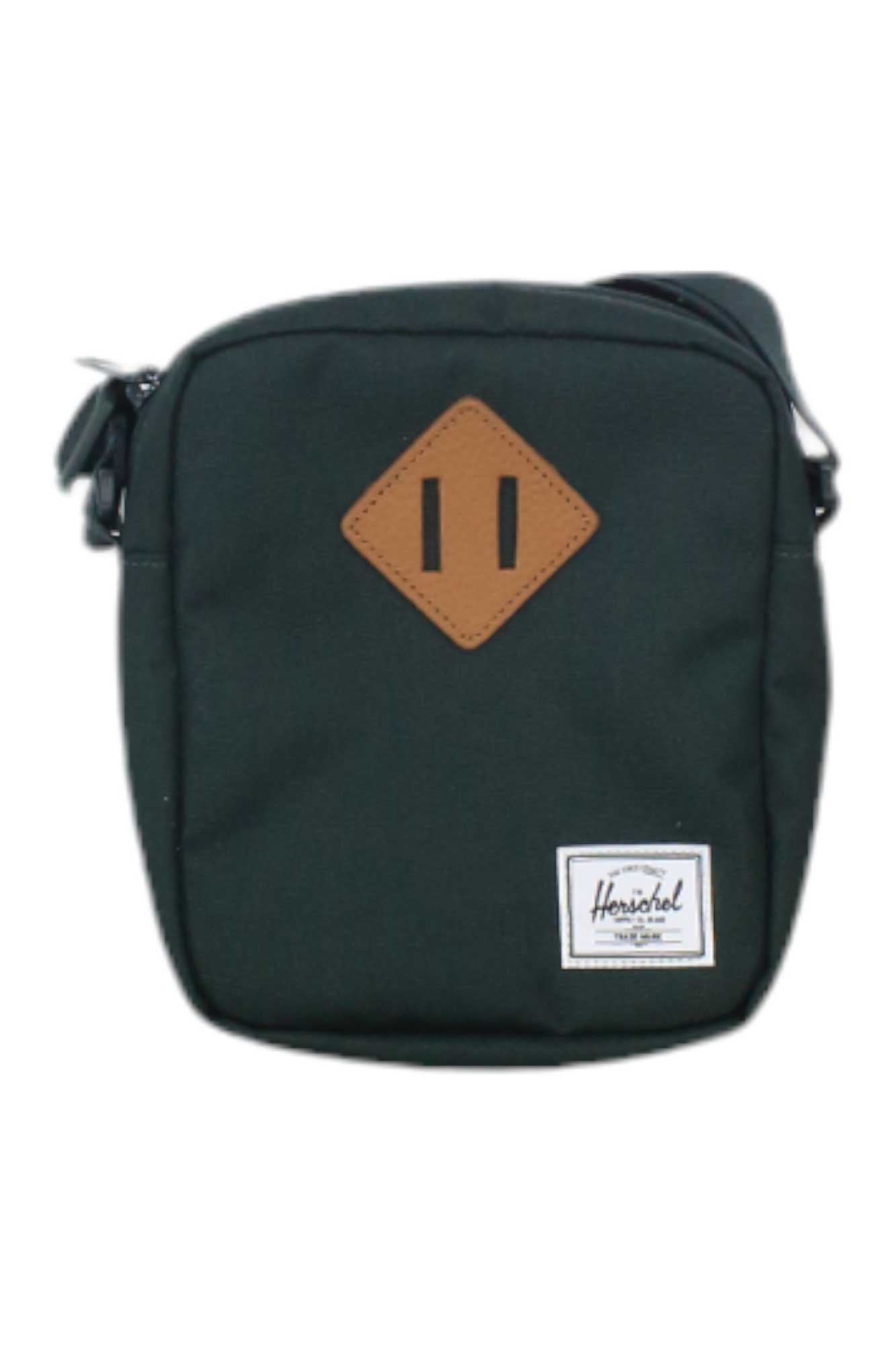 The Herschel Supply Company Heritage Crossbody Bag is small, rectangular, and dark green, made from EcoSystem recycled fabric with a brown leather diamond patch and a white Herschel label on the front.