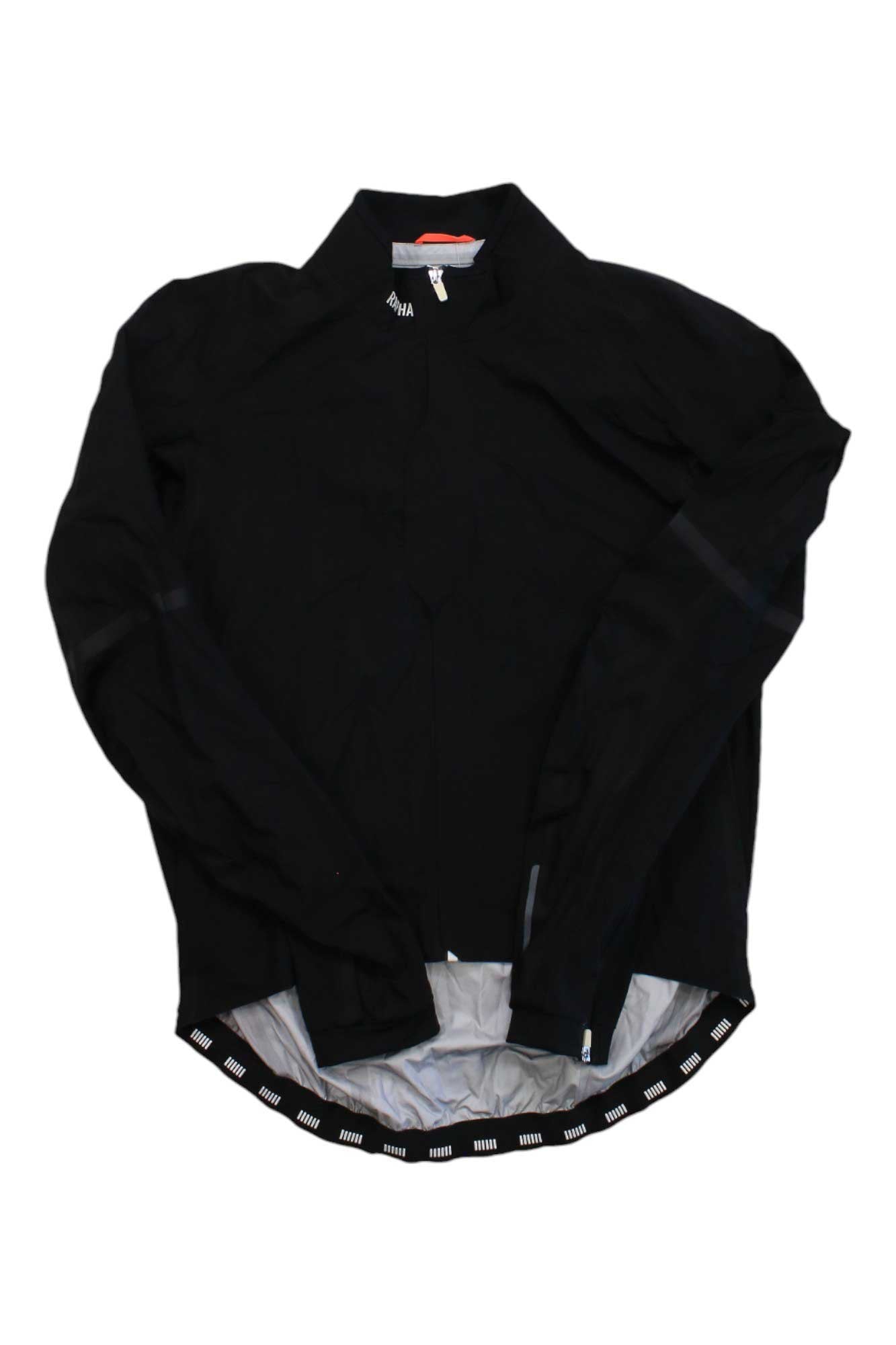 The Pro Team Race Cape is a lightweight, long-sleeve black cycling jacket with a high collar, reflective trim, interior lining, and an elastic hem with white markings, shown flat against a white background.