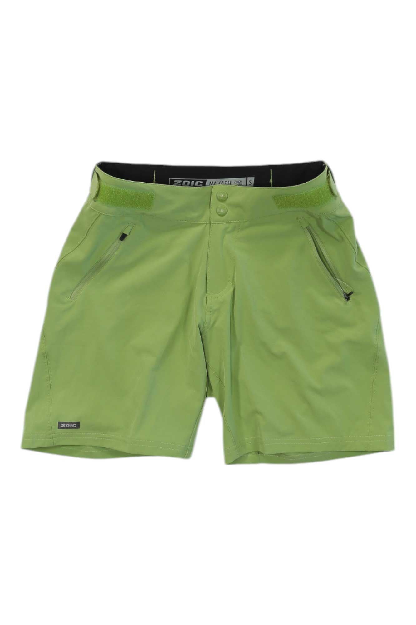 The Zoic Womens Navaeh 7 Short is a light green cycling short for women featuring zippered side pockets, button and Velcro front closure, and a subtle brand label on the lower left leg. These packable shorts are displayed on a white background.