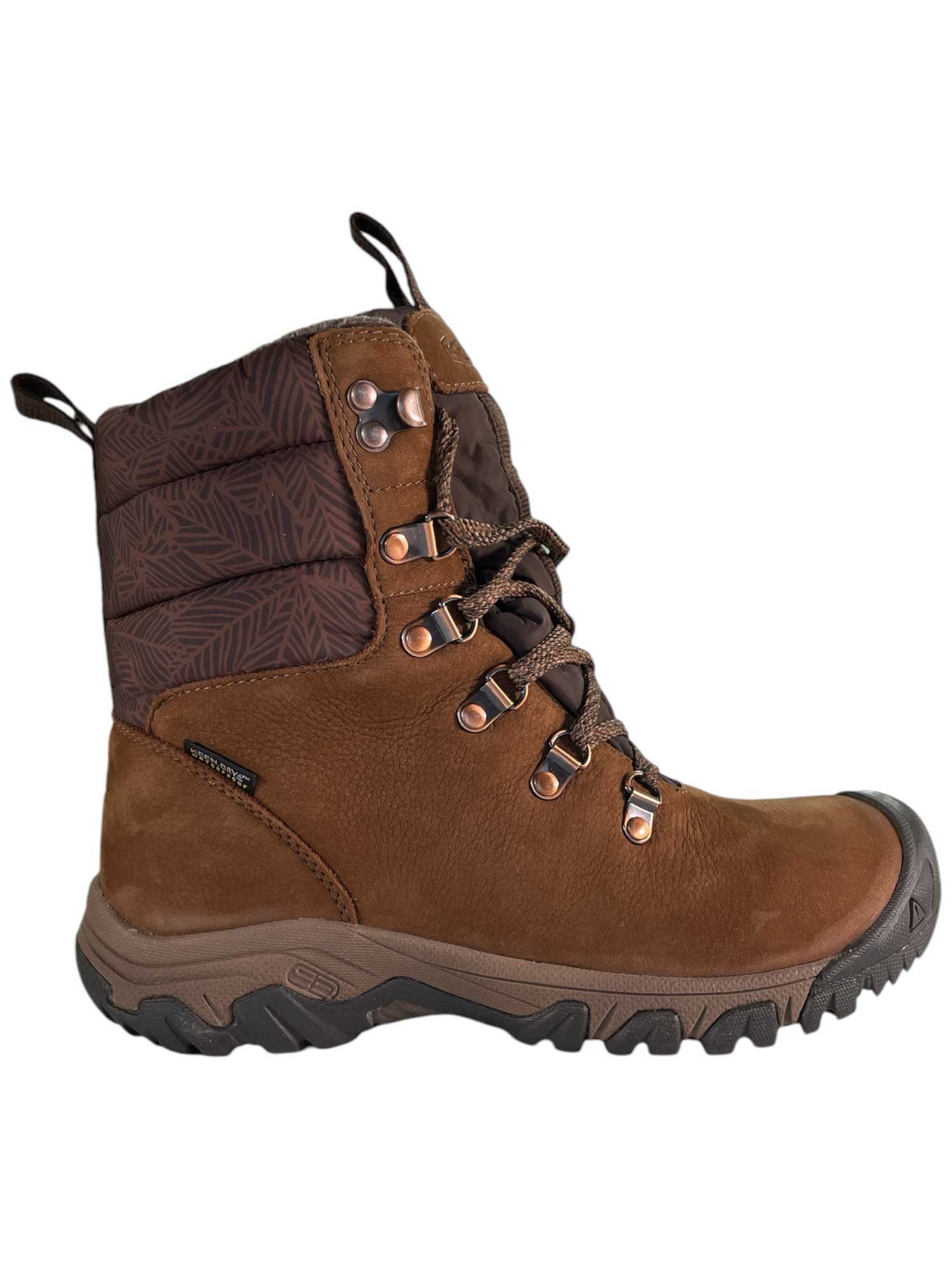 The KEEN Womens Greta Waterproof Boot is brown with dark patterned ankle padding, metal eyelets, and a rugged black and brown rubber sole. It has a lace-up front, pull tabs at tongue and heel, thermal insulation, and a textured outdoor-ready design.