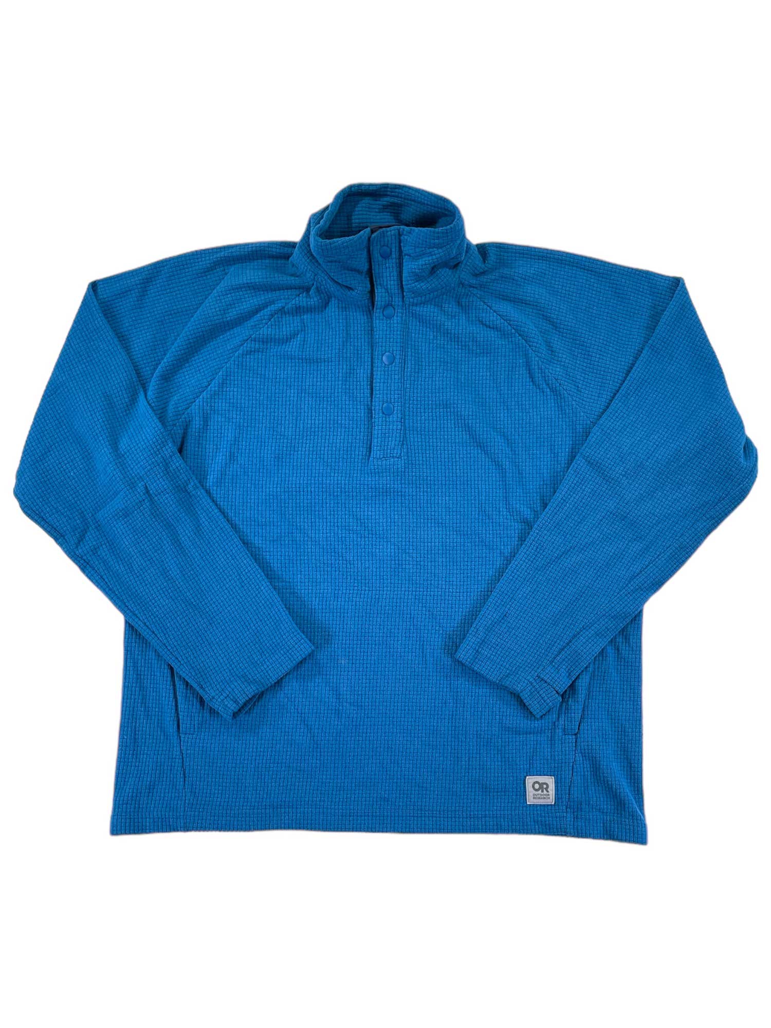 The Mens Trail Mix Snap Pullover is a blue, long-sleeve shirt with a stand-up collar, button placket, gridded fleece fabric for comfort, and a small rectangular patch near the bottom hem.