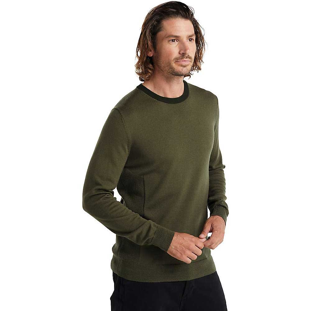 A man with medium-length brown hair and facial hair wears the Icebreaker Mens Shearer Crewe Sweater in olive green with black pants, standing against a plain white background—ideal for layering outdoors.
