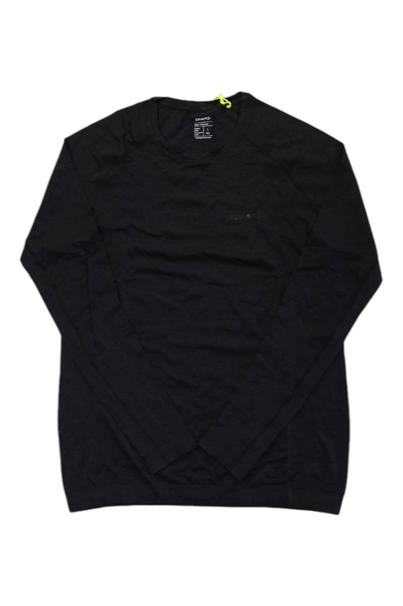 The Craft Sportswear Mens Core Dry Active Comfort LS Top, a plain black long-sleeve crew neck baselayer, is laid flat on a white background. A small neon yellow tag by the neckline highlights its comfortable active outdoor design.