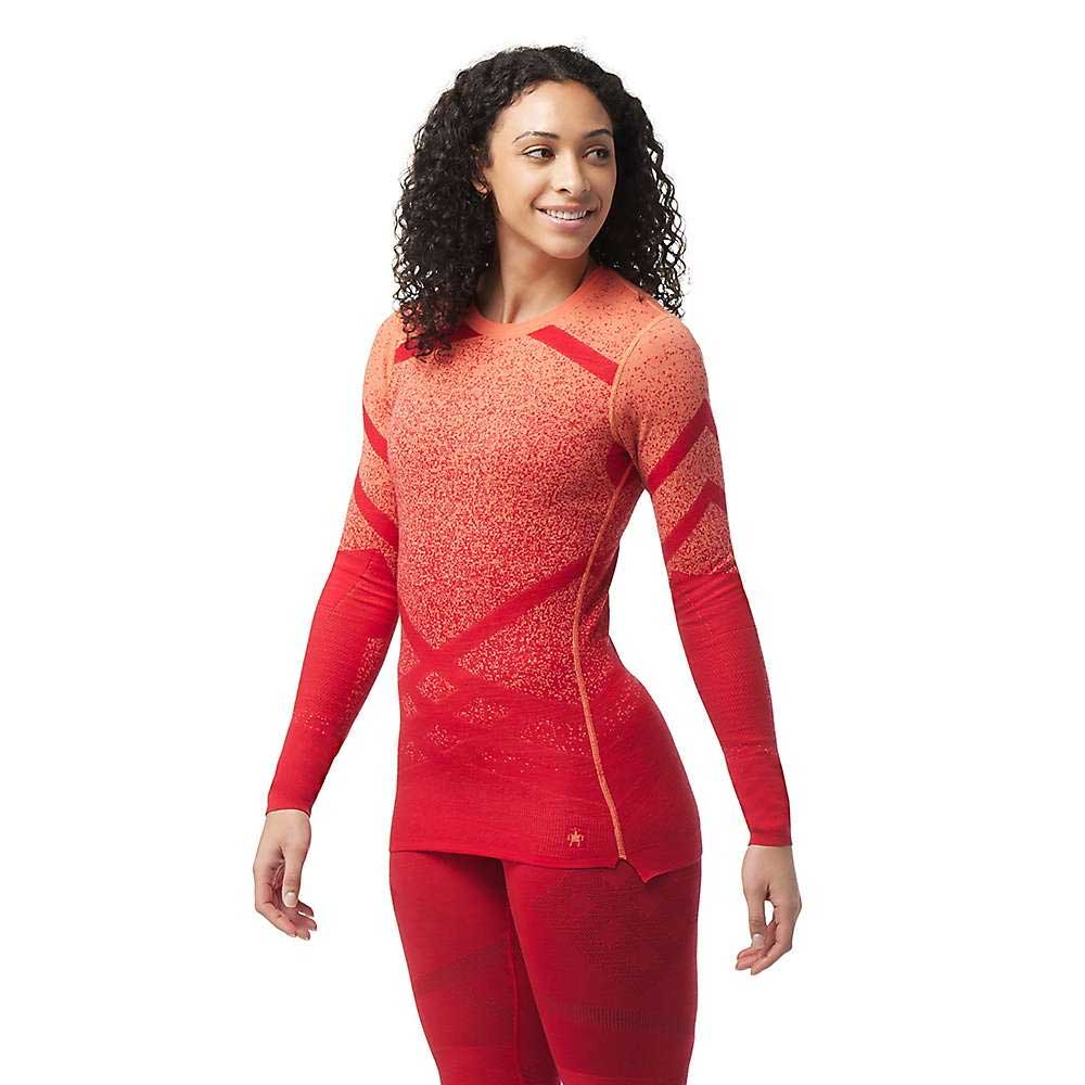A woman with curly hair smiles against a plain white background, wearing the Smartwool Womens Intraknit Thermal Merino Base Layer Pattern Crew and matching leggings.